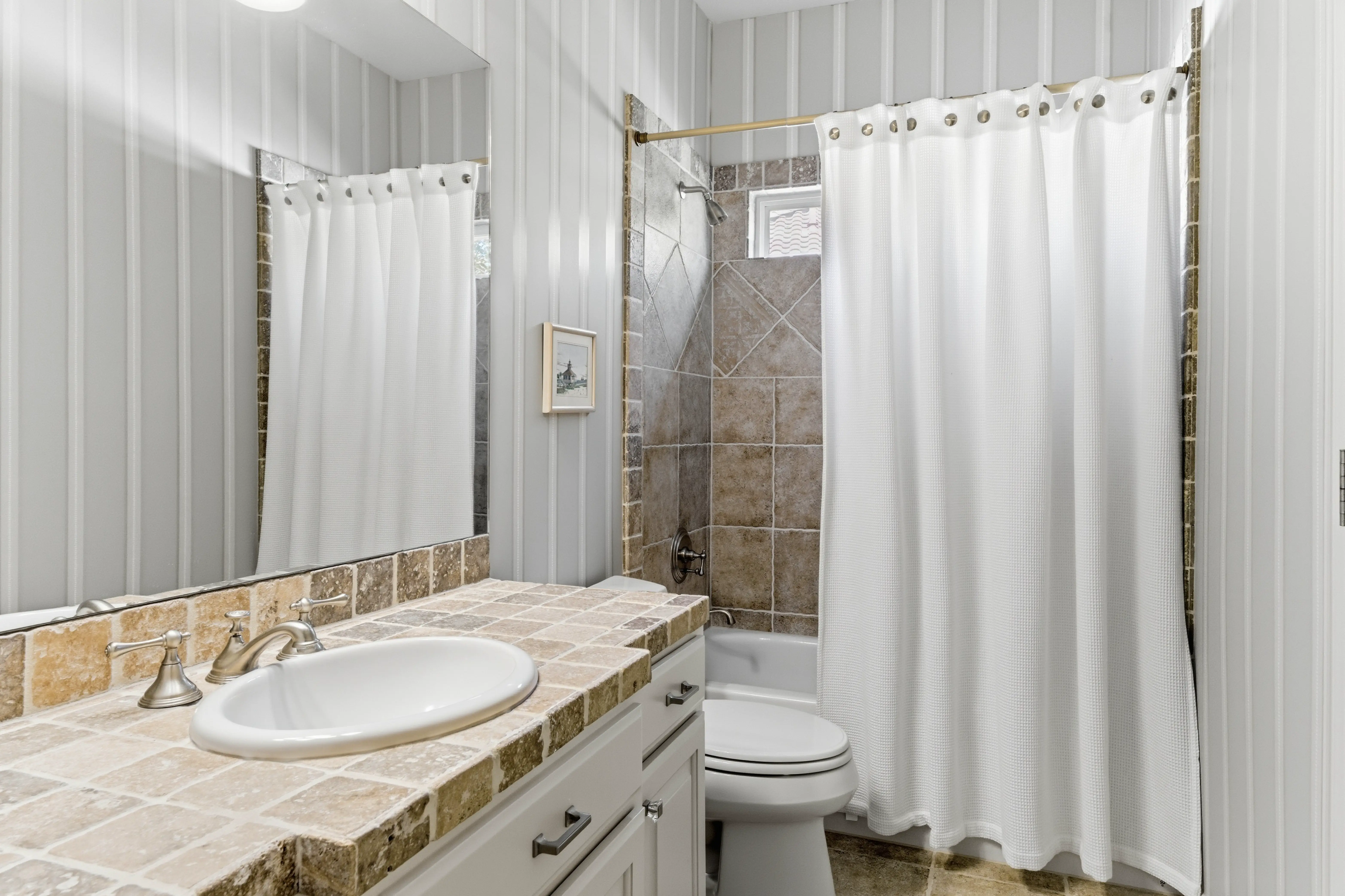 Guest bathroom with striped wallpaper, tile shower-tub combo, and single vanity
